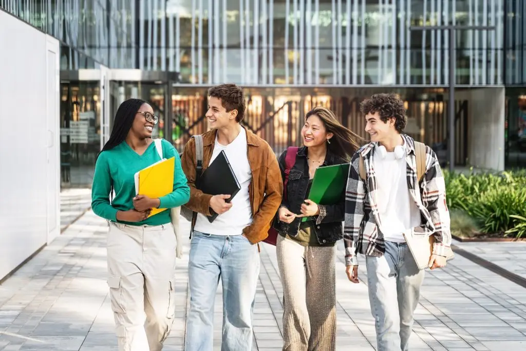 Four students walking across campus together carrying folders