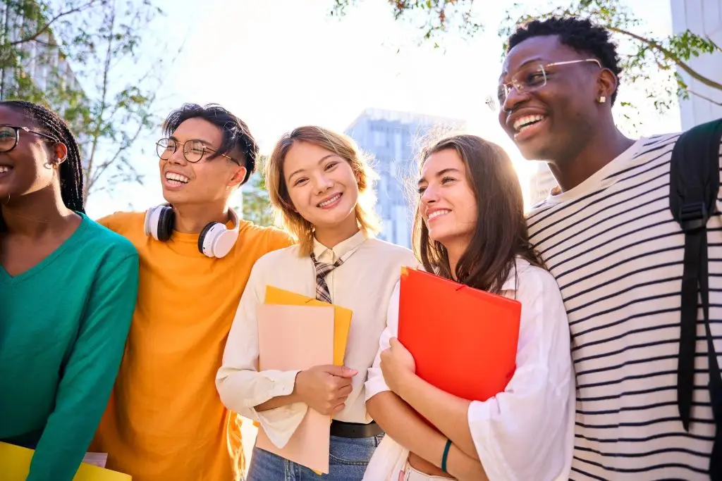 Five students standing together outdoors holding folders and notebooks