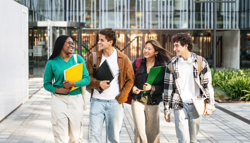 Four students walking across campus together carrying folders