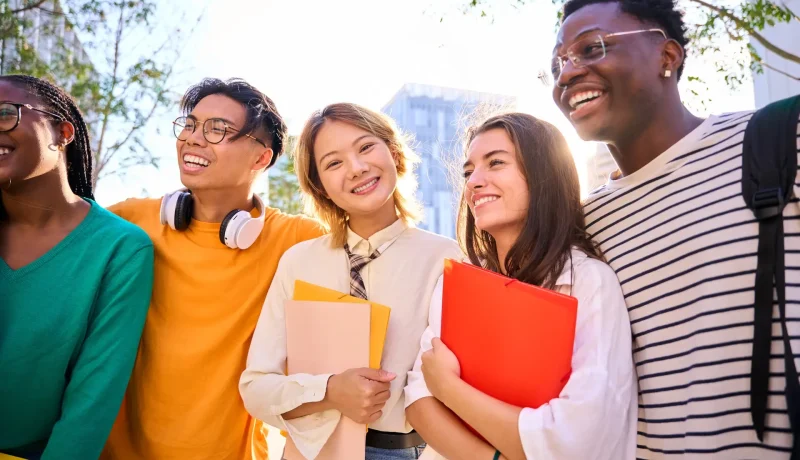 Five students standing together outdoors holding folders and notebooks